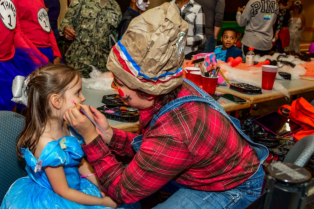 A sailor in a costume paints a child's face.