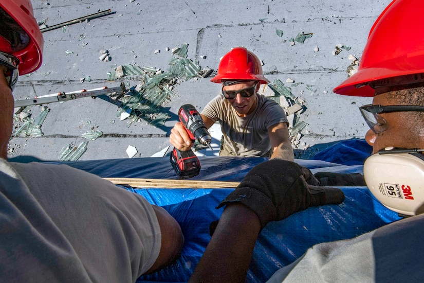 Air Force civil engineers use hand tools to repair a roof.
