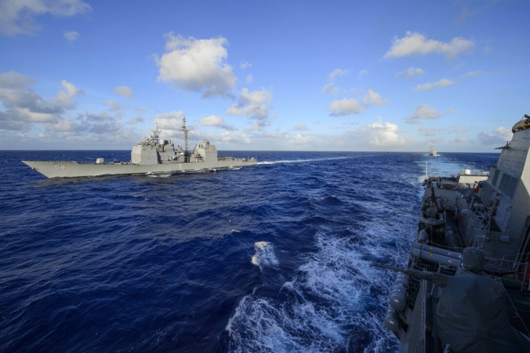 Three ships travel in blue waters.