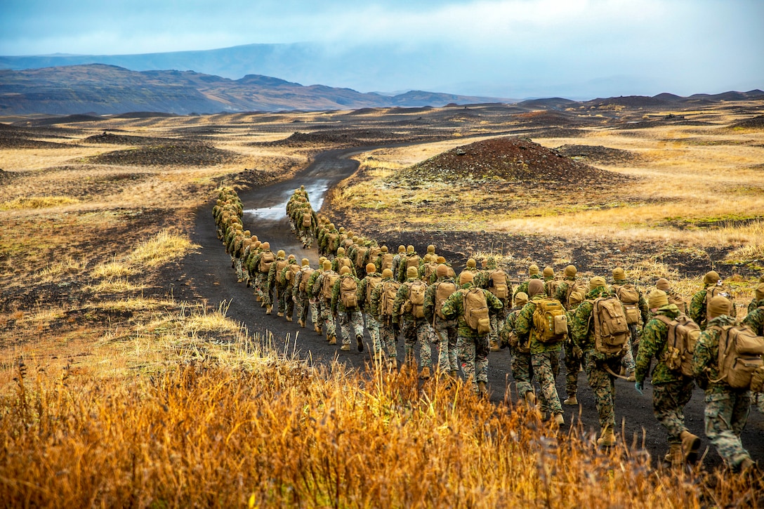 Marines hike across the flat landscape of Iceland as mountains loom in the distance.