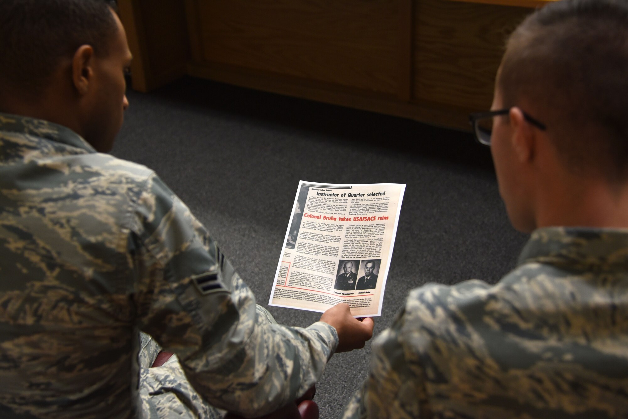 316th Training Squadron students look at a news article from the U.S. Air Force School of Applied Cryptologic Sciences Change of Command ceremony before the 60-year anniversary of intelligence training in the Piper Auditorium at Sebers Hall on Goodfellow Air Force Base, Oct. 19, 2018. The article features retired U.S. Air Force Col. Harlan Bruha taking control of the USAFSACS and he was the guest speaker for the 60-anniversary ceremony. (U.S. Air Force photo by Staff Sgt. Joshua Edwards/Released)