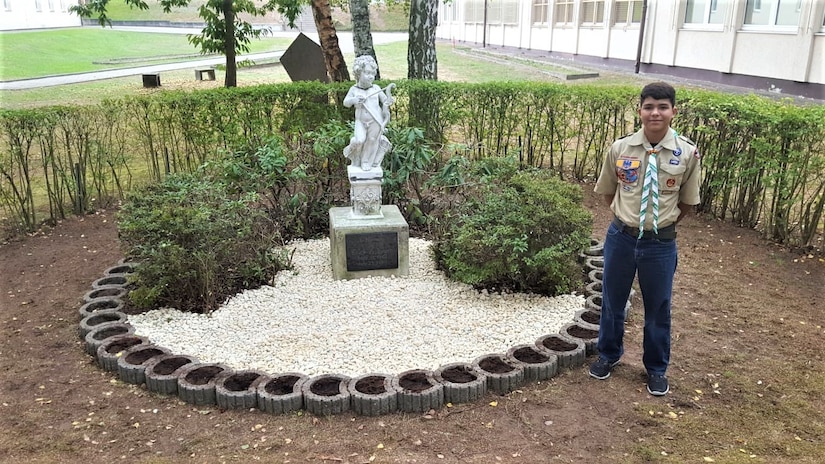 Nathan Perez poses at the newly restored memorial to the late Erick Lynch on October 6, 2018, at what is now Kaiserslautern Middle School.  Lynch was a Kaiserslautern American High School student killed in a hiking accident in 1998.  For his Eagle Scout project, Perez led a small group of his Boy Scout Troop 232 fellows and their parents in the restoration project. The memorial had fallen into neglect over the years. (US Army Reserve Photo by Sgt. 1st Class Juan Perez)