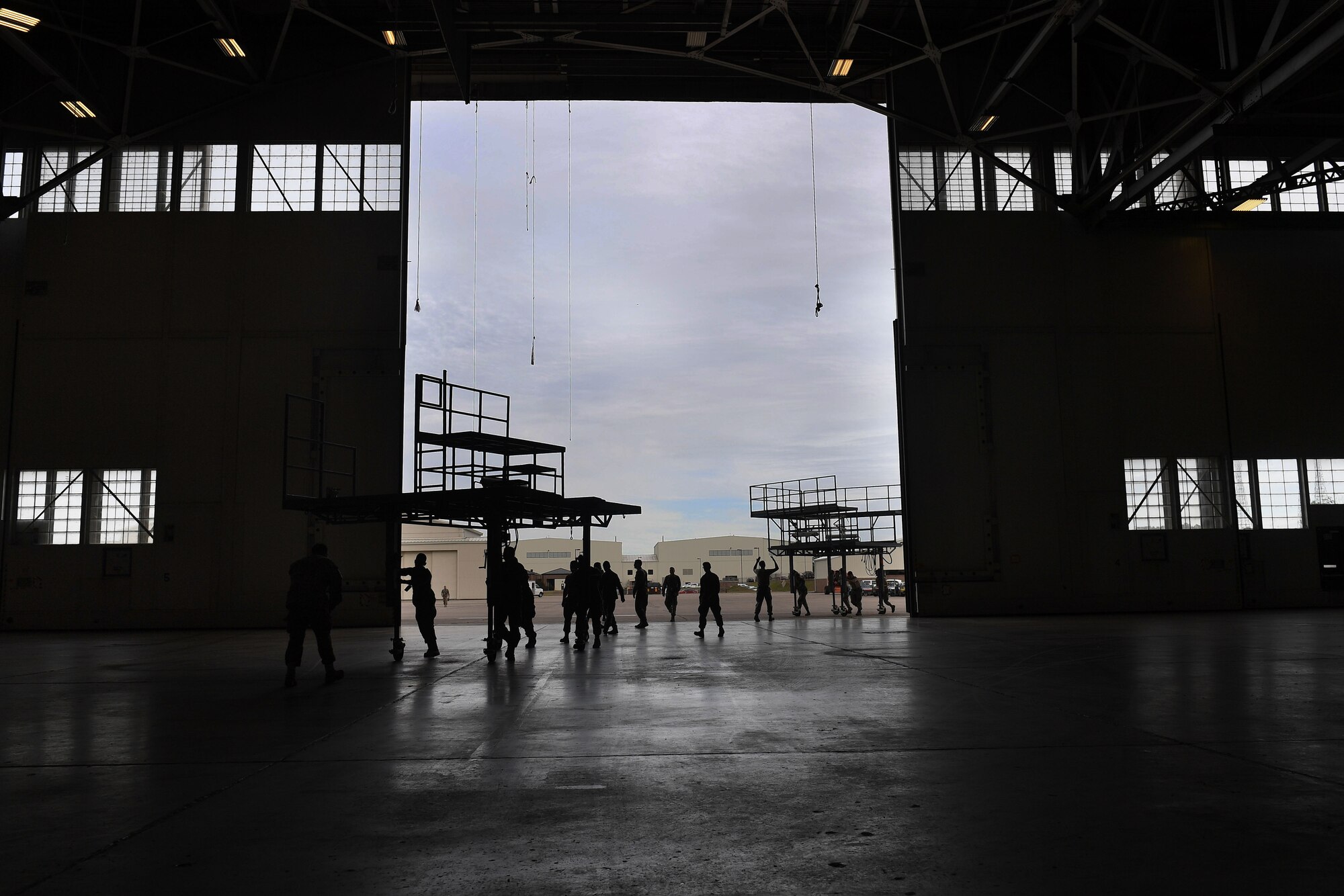A group of people work in together to move stands through the entryway of a hangar.