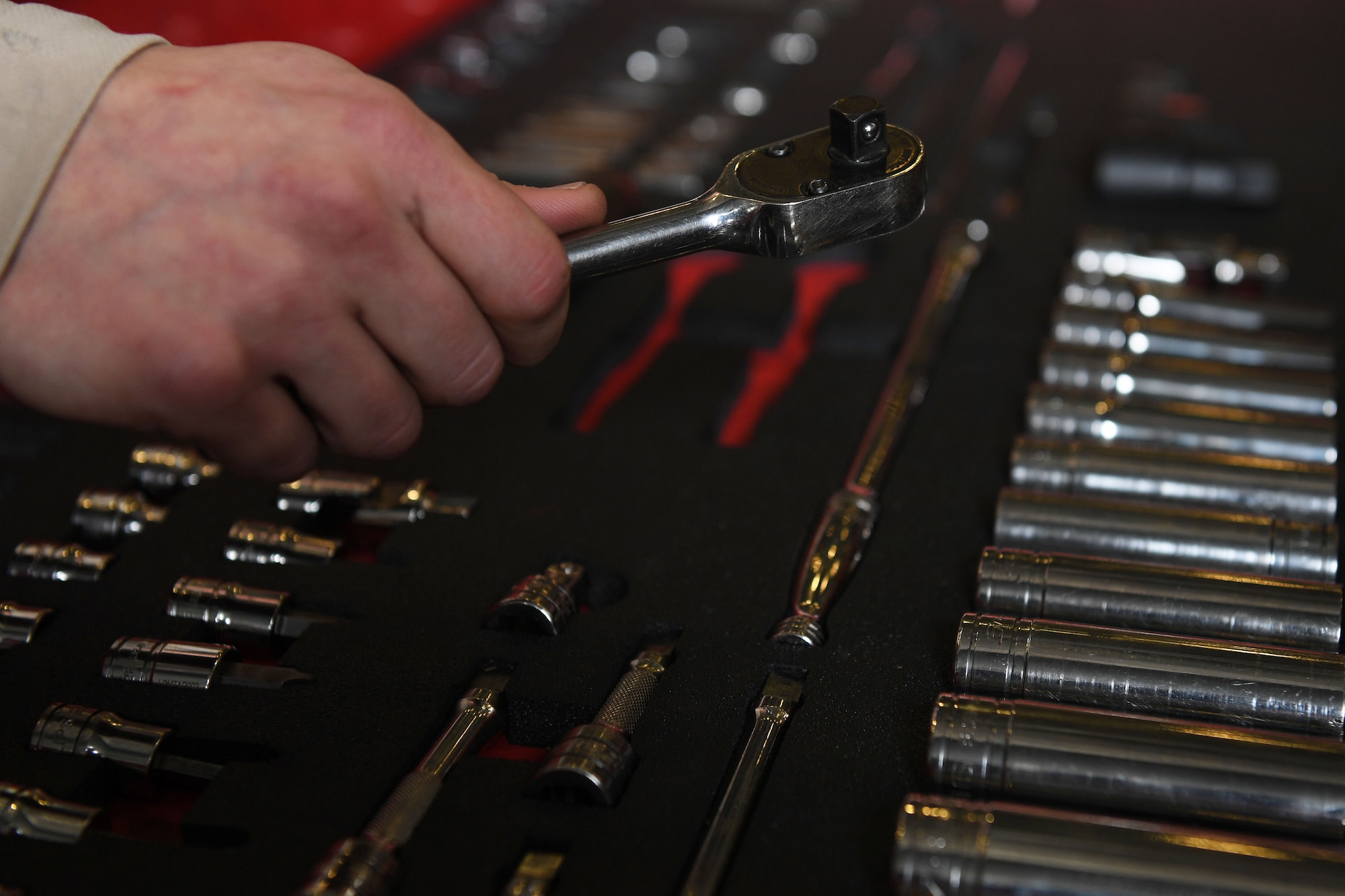 A hand holds a tool over an open toolbox.