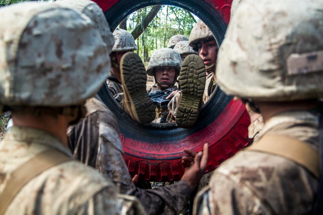 A Marine goes feet first through a tire that fellow Marines are holding up.