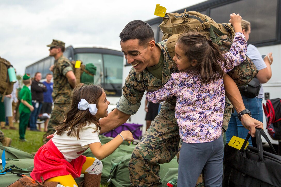 One little girl hugs a smiling Marine as he reaches down to hug another one.