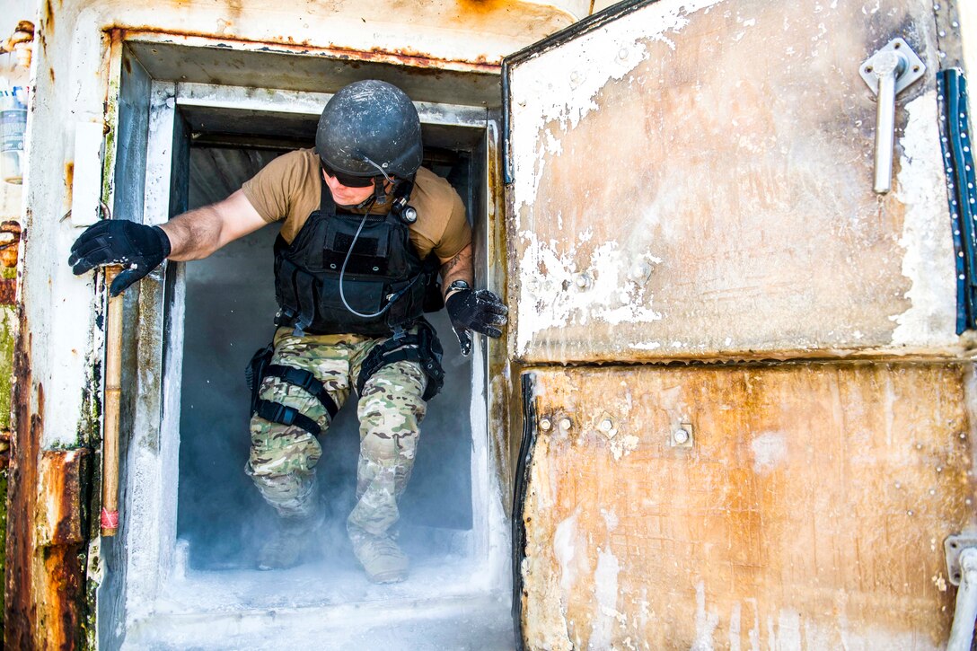 A sailor bends down to step out of a refrigerator, as smoke wafts around his feet.