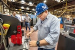 Jeff Pugh, a pipefitter, uses a new 3D-printed alignment tool to help punch holes in an iron pipe hanger.