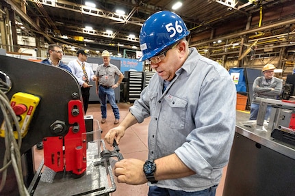 Jeff Pugh, a pipefitter, uses a new 3D-printed alignment tool to help punch holes in an iron pipe hanger.