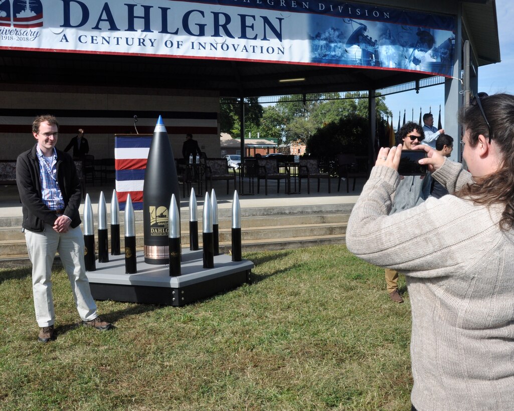 IMAGE: DAHLGREN, Va. (Oct. 19, 2018) – Dahlgren personnel take pictures with the time capsule at the Naval Surface Warfare Center Dahlgren Division (NSWCDD) centennial grand finale. As participants celebrated Dahlgren’s impact upon the Navy and nation, the time capsule – ten 105 millimeter shells surrounding a 16-inch shell –  was unveiled and all in attendance had the opportunity to write notes and share their thoughts with future generations. Dahlgren personnel can write notes to be placed inside the capsule until the end of 2018 when it will be sealed and opened on Oct. 16, 2068 at the command’s 150th anniversary.