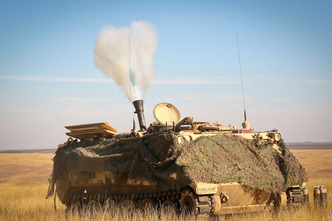 A mortar round shoots from a tracked vehicle. in a field.
