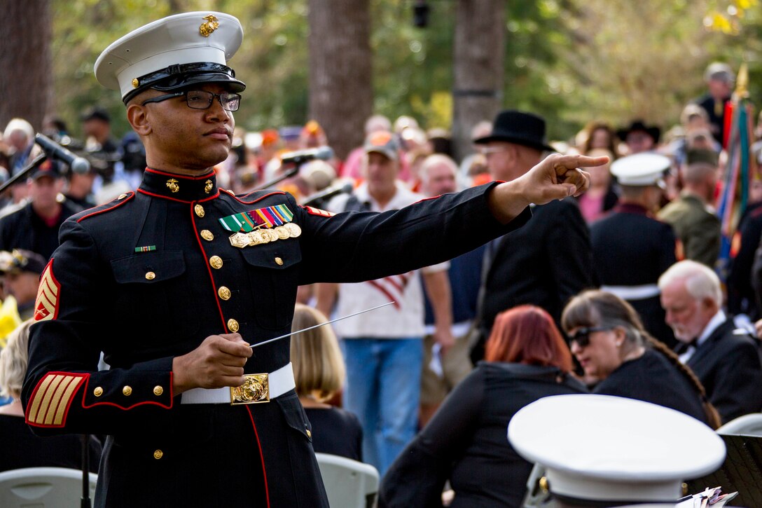 A Marine conducts a band with people in the background.