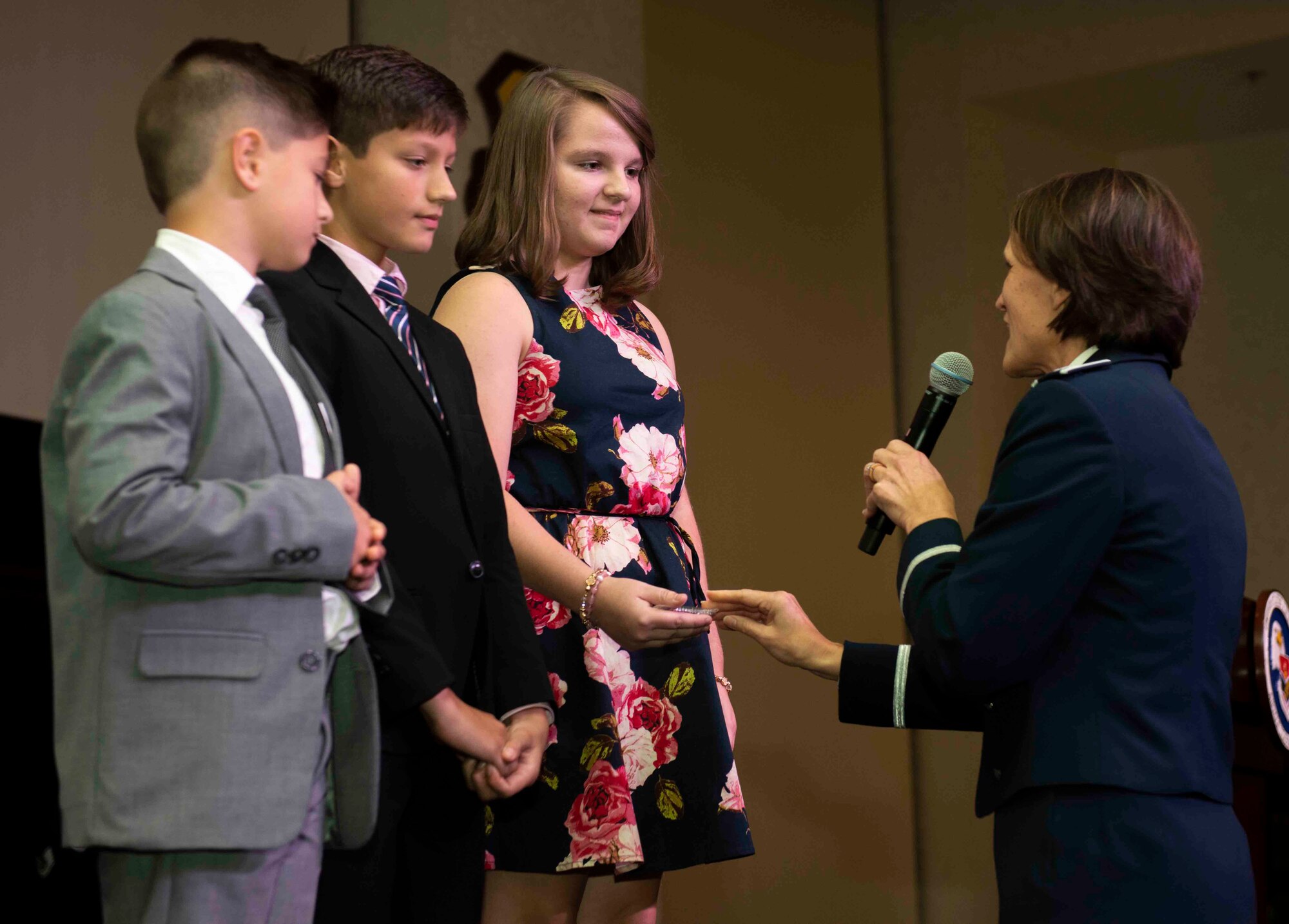 Eliana, Tristan and Caleb, children of fallen Master Sgt. Gregory Kuhse from the 3rd Manpower Requirements Squadron, receive coins from Col. Leslie Maher, 357th Air Mobility Wing commander, at the Class 18-G Airman Leadership School graduation, Oct. 11. This moment was part of the school’s new legacy project meant to honor past service members. (U.S. Air Force photo by Senior Airman Tara Stetler)