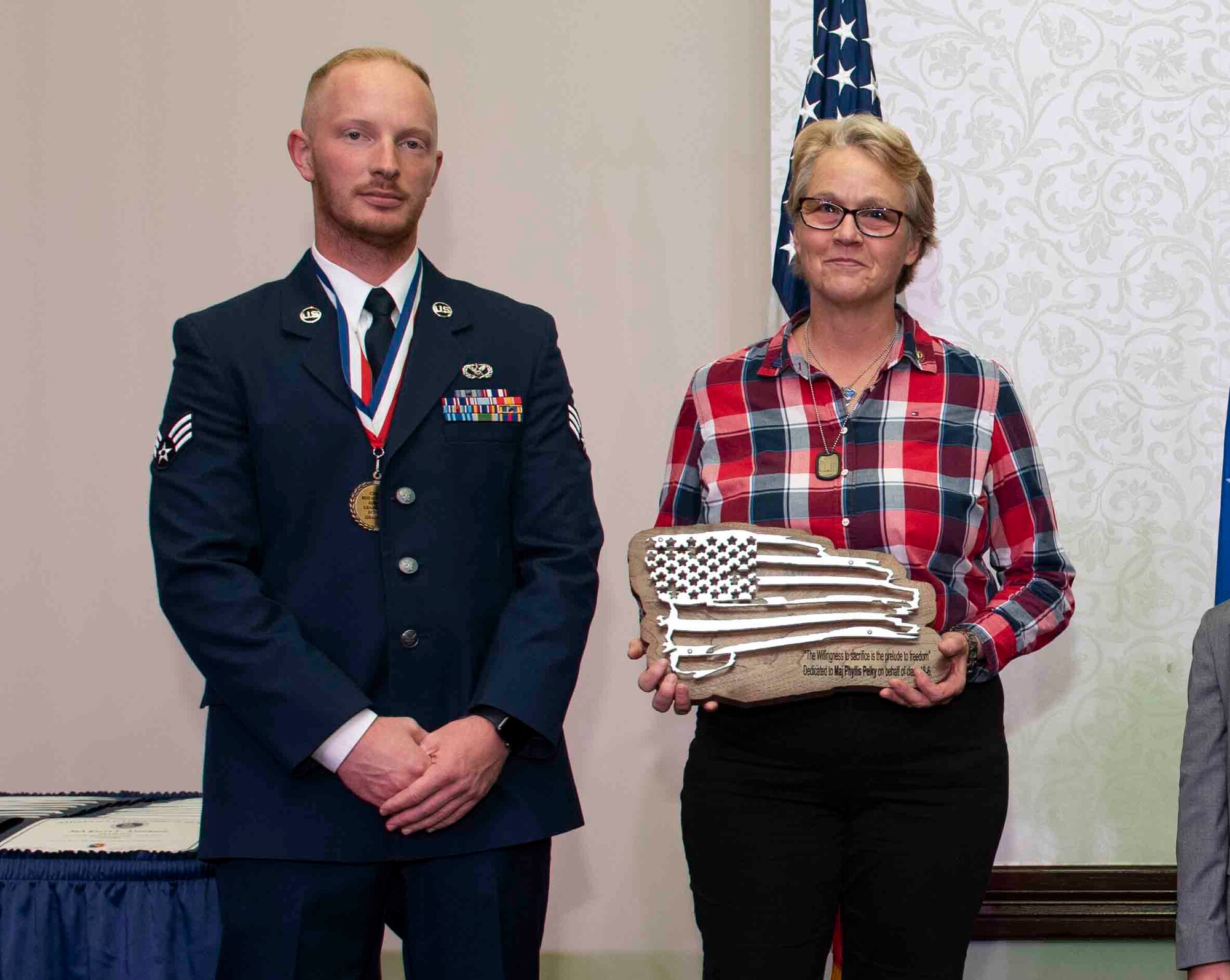 Senior Airman Payton Long, 375th Civil Engineer Squadron structural apprentice, presents Cathy Berlin-Obregon a plaque honoring her sister, Air Force Academy instructor Maj. Phillis Pelky, at the Class 18-G Airman Leadership School graduation. Pelky was killed in a 2015 helicopter crash in Afghanistan, which also took the life of Kuhse. (U.S. Air Force photo by Senior Airman Tara Stetler)