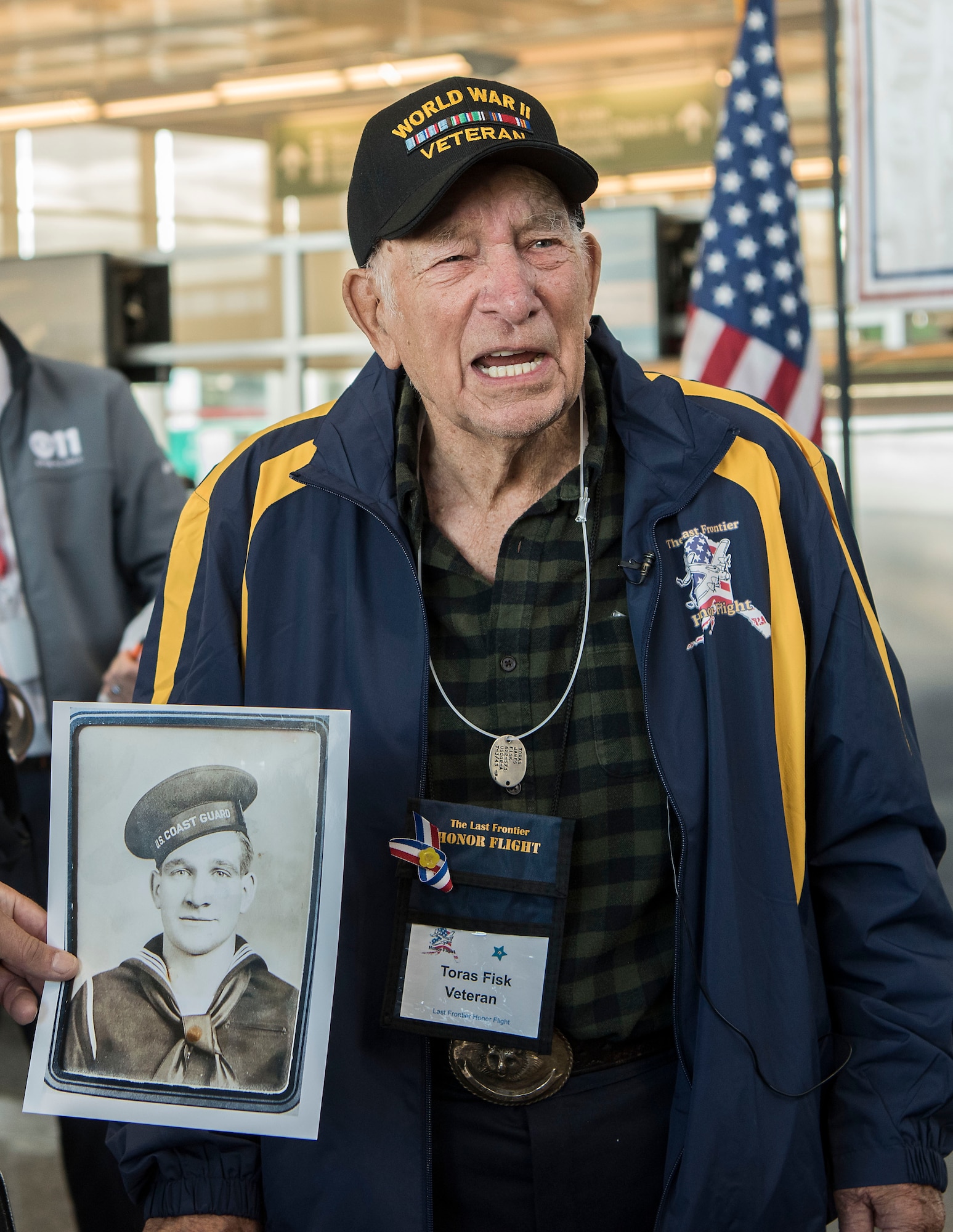 Toras Fisk, a World War II veteran, stands by an official military photo of himself, at Ted Stevens International Airport, before leaving for Washington, D.C., with the Last Frontier Honor Flight, Alaska, Oct. 16, 2018. The program offers veterans the opportunity to visit monuments erected in their honor such as the National World War II Memorial, the Korean War Veterans Memorial and the Vietnam Veterans Memorial.