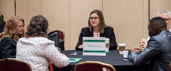 Job seekers chat at a table with NSA representatives about opportunities in computer science at NSA.