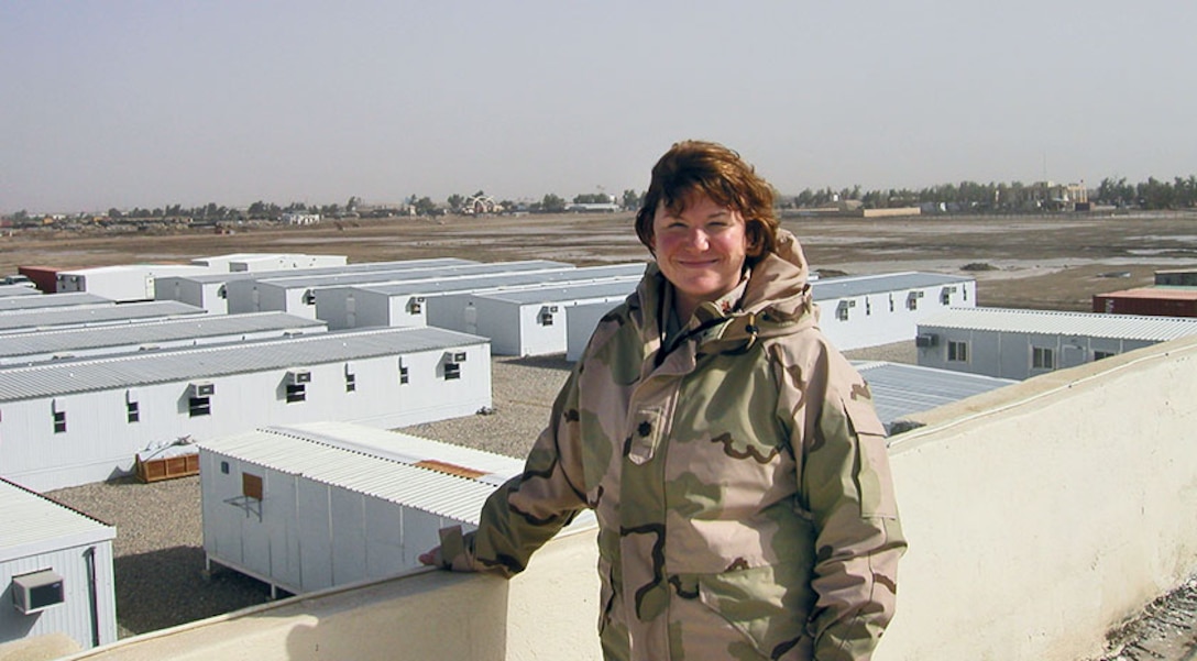 Becky stands on a rooftop overlooking small buildings in a desert town