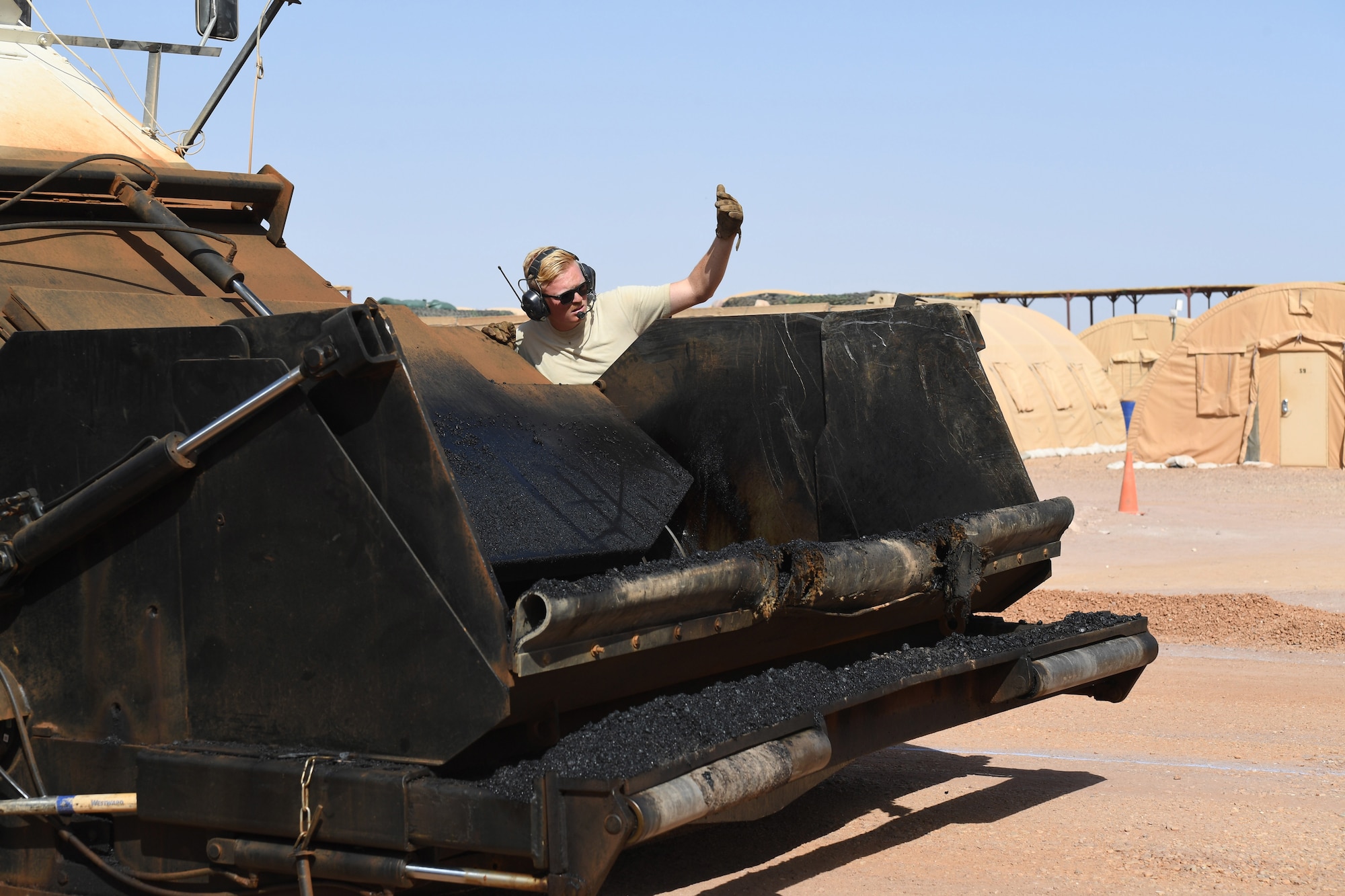 U.S. Air Force Airman 1st Class Conner Roberts, 31st Expeditionary Rapid Engineer Deployable Heavy Operation Repair Squadron Engineer pavement and equipment journeyman, signals to the dump truck to start loading the Material Transfer Vehicle with asphalt at Nigerien Air Base 201, Agadez, Niger, Oct. 19, 2018. The MTV allows Airmen to pave continuously with well-mixed asphalt. (U.S. Air Force photo by Tech. Sgt. Rachelle Coleman)