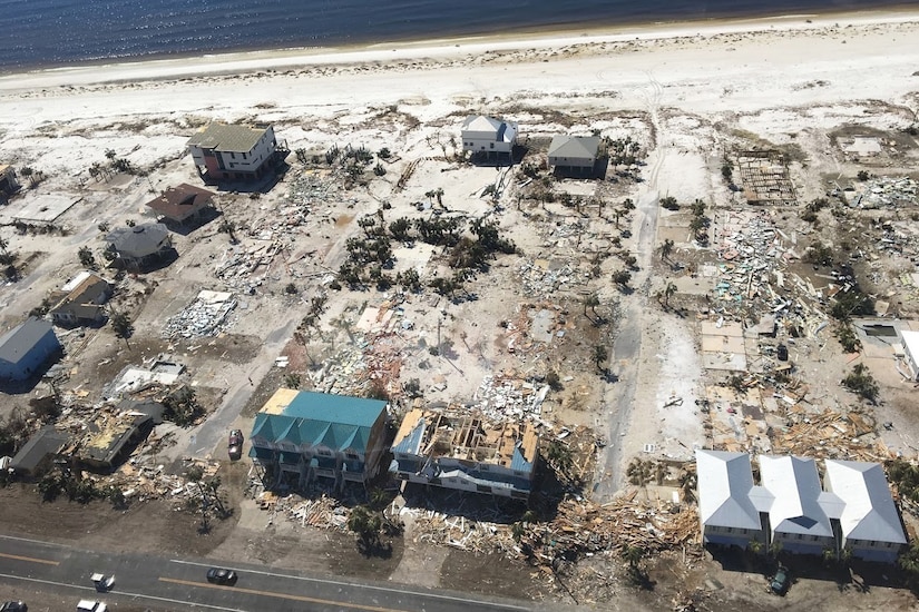 An aerial view shows devastated buildings along a sandy coast.