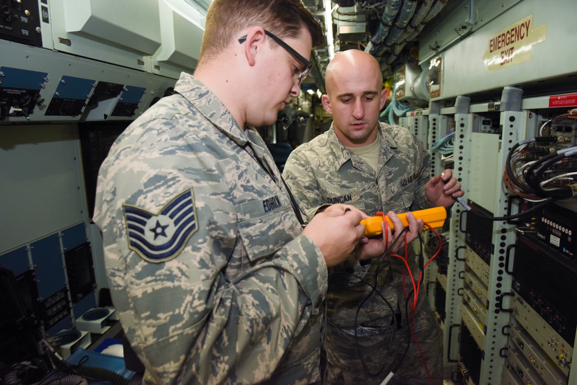 U.S. Air Force Tech. Sgt. Brett Edholm, 95th Reconnaissance Squadron, electrical warfare systems NCO- in-charge, and Staff Sgt. Randy Duncan, 95th RS RC-135 Rivet Joint electronic warfare craftsman, check the voltage on loose fiber optic cables on a RC-135 Rivet Joint at RAF Mildenhall, England, Oct. 16, 2018.