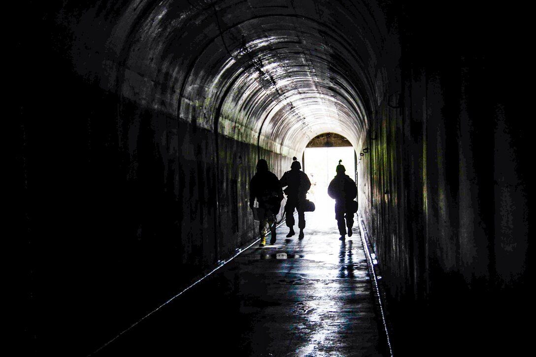 Three figures, shown in silhouette, walk in a dark tunnel