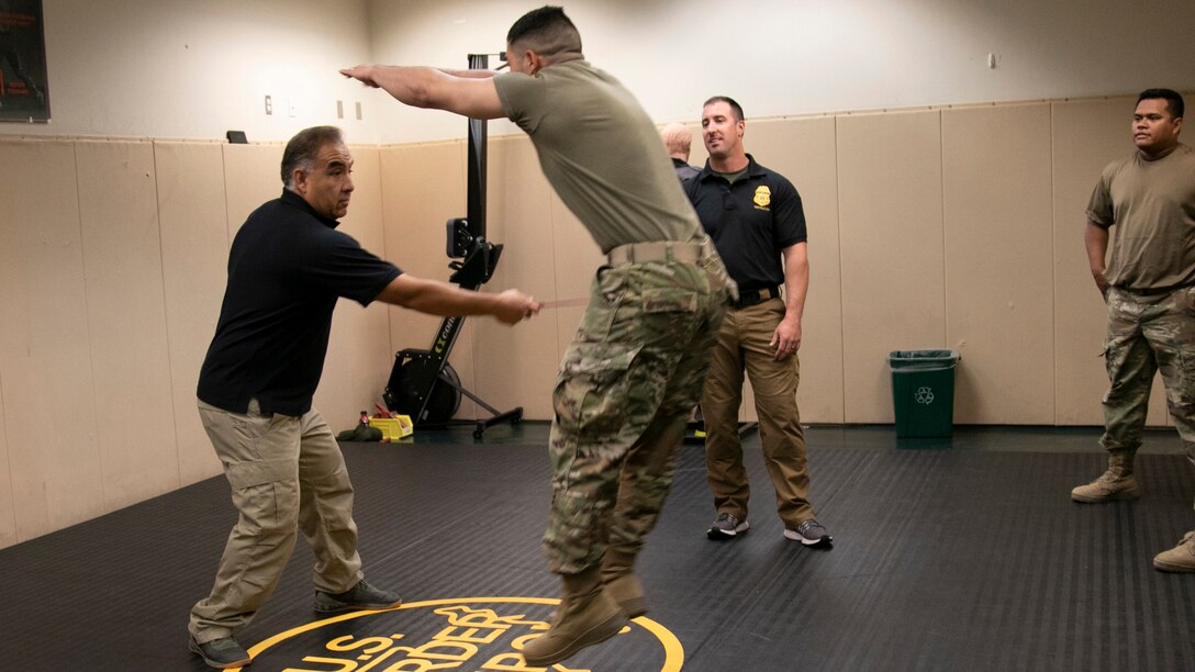 A guardsman jumps back as an instructor moves toward him with a sharp object in a gym.