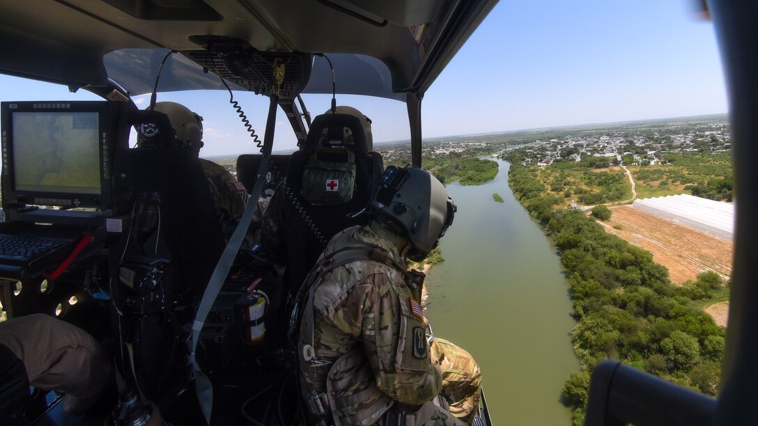 Guardsmen in an aircraft fly over a river.