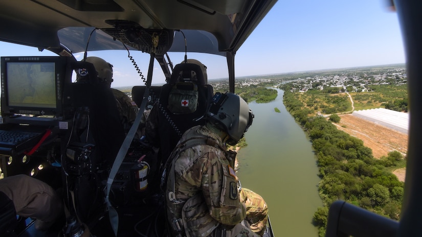 Guardsmen in an aircraft fly over a river.