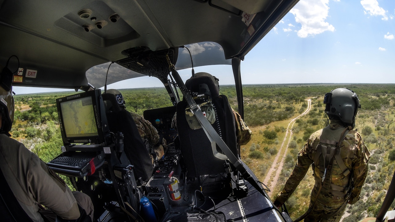 Guardsmen in an aircraft look out over the terrain.