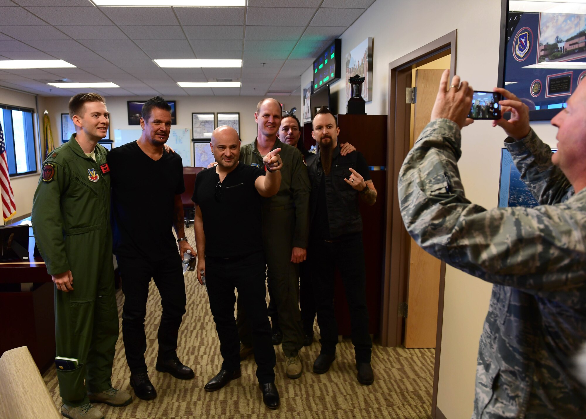 Disturbed band members take a photo with 432nd Wing/432nd Expeditionary Wing pilots in wing headquarters at Creech Air Force Base, Nevada, Oct. 23, 2018. Disturbed came to Creech via the USO and performed a concert for Airmen after learning about the wing mission. (U.S. Air Force photo by Senior Airman Christian Clausen)