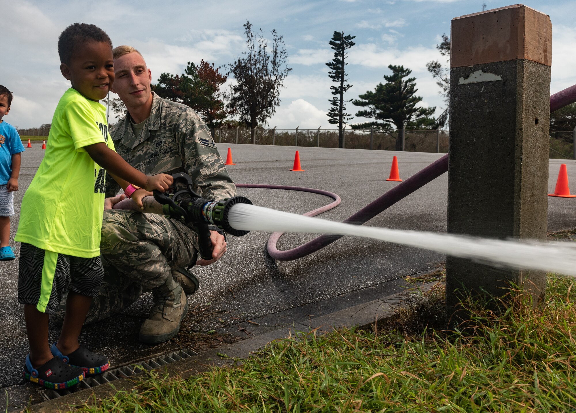 U.S. Air Force Airman 1st Class Jason Sansone, 18th Civil Engineer Squadron firefighter, helps a child use a fire hose during the Fire Station 1 Open House Oct. 6, 2018, on Kadena Air Base, Japan. The open house was hosted by the 18th CES to raise awareness about fire safety during Fire Prevention Week. (U.S. Air Force photo by Staff Sgt. Micaiah Anthony)