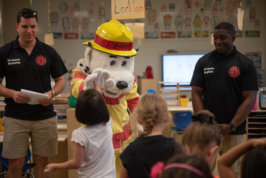 A child high-fives Sparky the Fire Dog before a fire safety briefing from U.S. Air Force Staff Sgt. Dominic Schultz, left, 18th Civil Engineer Squadron fire inspector, Tech. Sgt. Marshall Boykins, 18th CES NCO in-charge of fire inspections, Oct. 10, 2018, at Kadena Elementry School on Kadena Air Base, Japan. Firefighters from the 18th CES started Fire Prevention Week off with a proclamation signing followed by an open house at Fire Station 1, school visits, presentations, demonstrations, a fire muster and a parade. The events were designed to promote fire safety and awareness. (U.S. Air Force photo by Staff Sgt. Micaiah Anthony)
