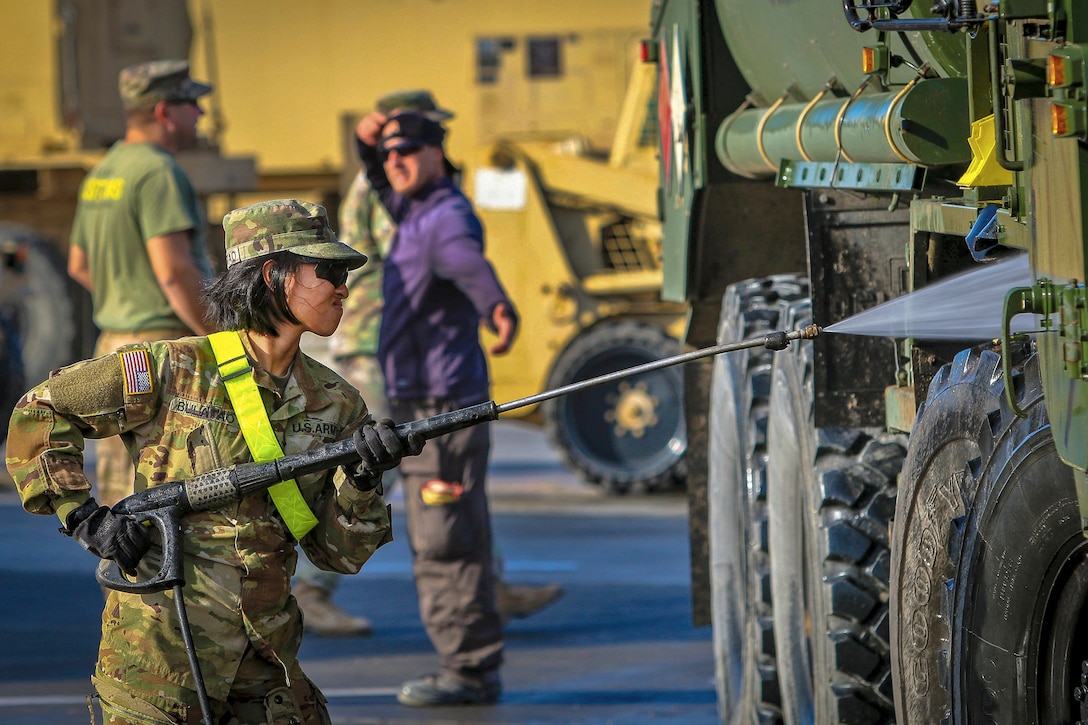 A soldier trains a water sprayer on a vehicle's undercarriage.