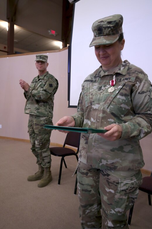 Command Sgt. Maj. Sara E. Noskowiak, outgoing U.S. Army Reserve Music Sergeant Major, 88th Readiness Division, smiles proudly at her Meritorious Service Medal, given to her by Maj. Gen. Patrick J. Reinert, 88th Readiness Division commanding general, during the U.S. Army Reserve Music change of responsibility ceremony at Fort McCoy, Wisconsin, October 20, 2018. Her successor, Master Sgt. Keith M. Barlow, applauds behind her. Noskowiak helped bring the position of U.S. Army Reserve Music Sergeant Major to the attention of U.S. Army Reserve Command by having all the readiness divisions sign a memorandum agreeing to support the position which manages all of the U.S. Army Reserve Music units.