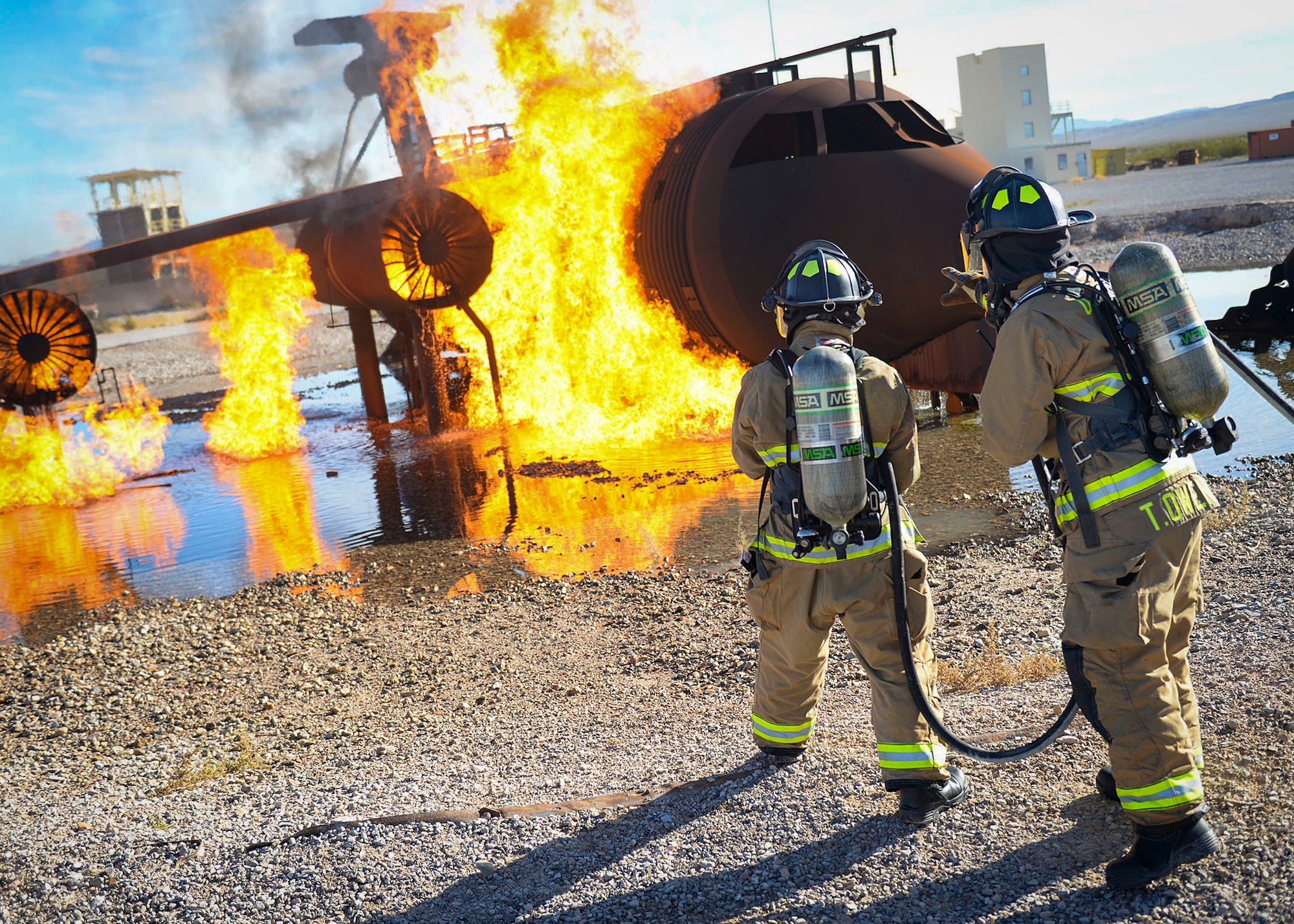 Airman Nigea Goodwin and Senior Airman Trevor Owens, both 99th Civil Engineer Squadron firefighters, approach a simulated aircraft fire at the fire department training area on Nellis Air Force Base, Nev., Oct 23, 2018. Real-life jet fuel can burn at over 1,800 degrees Fahrenheit so propane is used during the training for safety purposes. (U.S. Air Force photo by Airman 1st Class Bryan T. Guthrie)