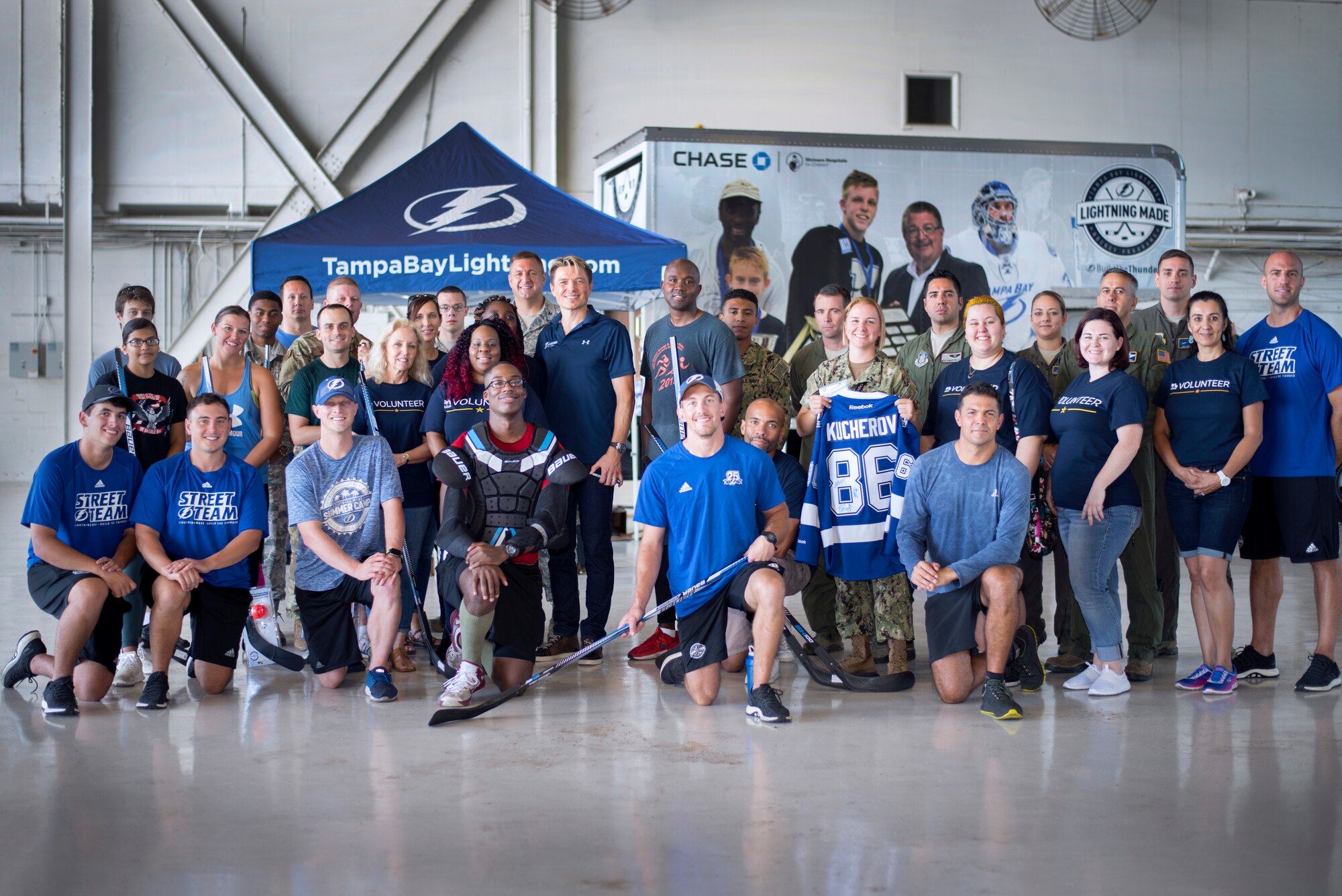 U.S. Air Force Airmen assigned to the 6th Air Mobility Wing, 927th Air Refueling Wing and U.S. Navy Seamen from Central Command, along with USAA volunteers, the Tampa Bay Lightning Street Team, and former Lightning players, Ruslan Fedotenko and Mathieu Garon, pose for a picture at Hangar 4 on MacDill Air Force Base, Florida, Oct. 25, 2018.