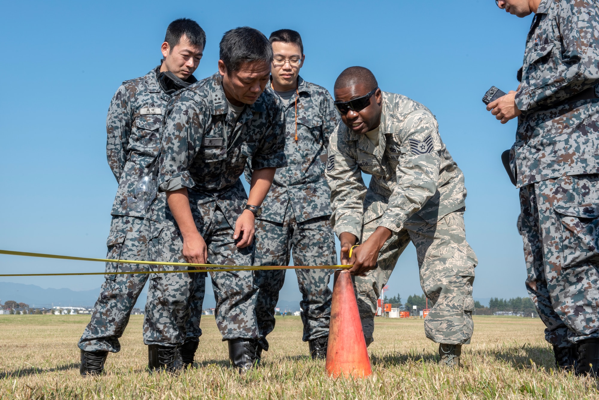 U.S. Air Force Tech. Sgt. Romain Smith, 374th Civil Engineer Squadron electrical power production, works with members of the Koku Jietai (Japan Air Self-Defense Force) members to measure out the proper positioning for the Mobile Aircraft Arresting System (MAAS) at a bilateral training event at Yokota Air Base, Japan, Oct. 25, 2018.