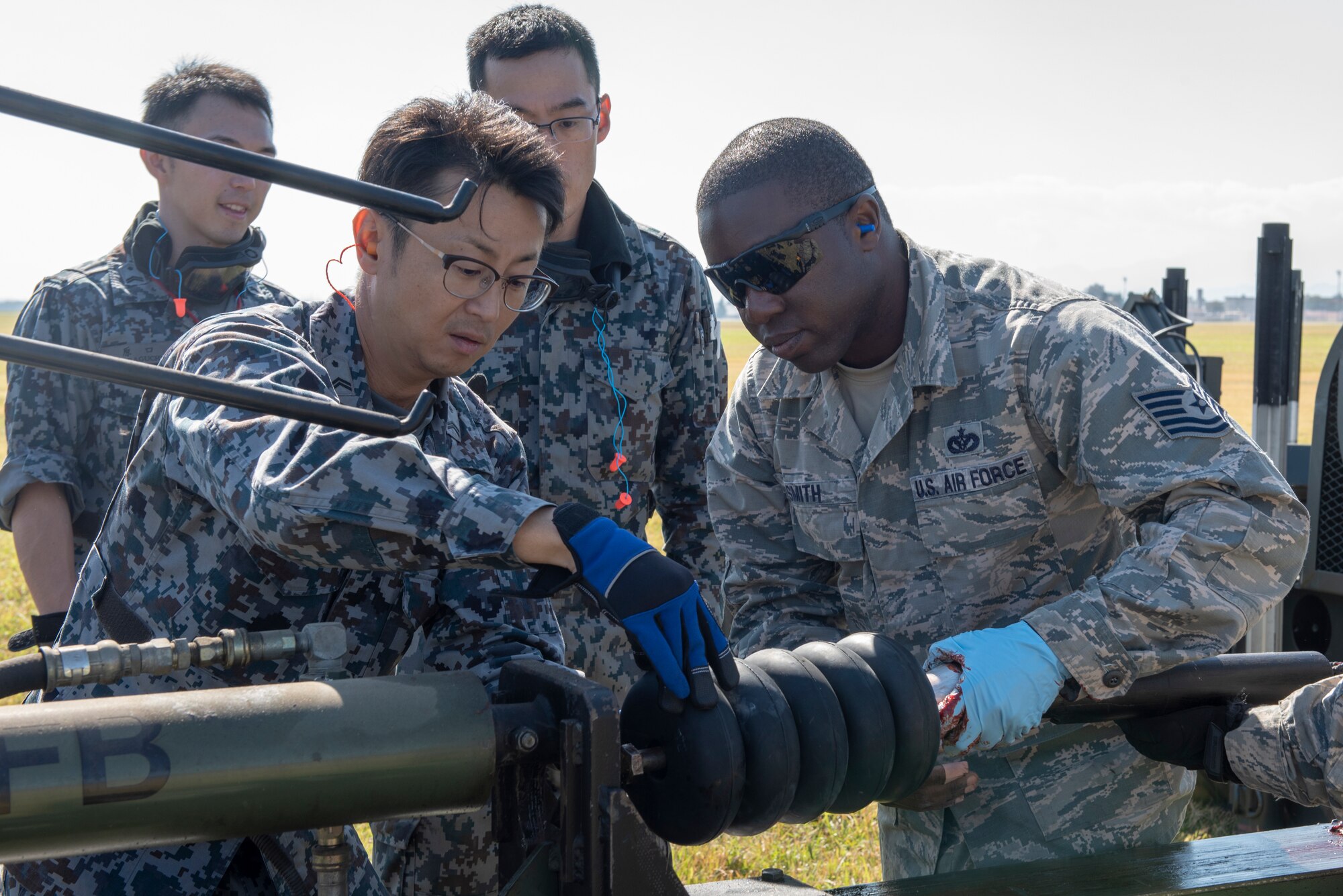 U.S. Air Force Tech. Sgt. Romain Smith, 374th Civil Engineer Squadron electrical power production, works with members of the Koku Jietai (Japan Air Self-Defense Force) members to install donuts onto the cable of a Mobile Aircraft Arresting System (MAAS) at a bilateral training event at Yokota Air Base, Japan, Oct. 25, 2018.