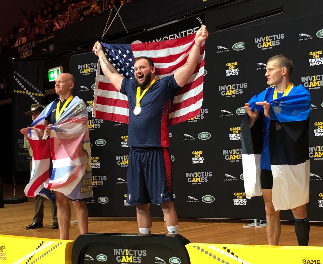 An athlete stands on a podium holding a flag.