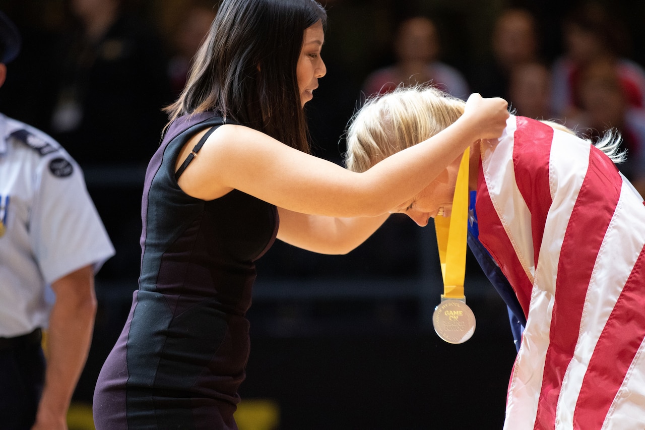 An athlete wearing an American flag bows down to receive a medal.