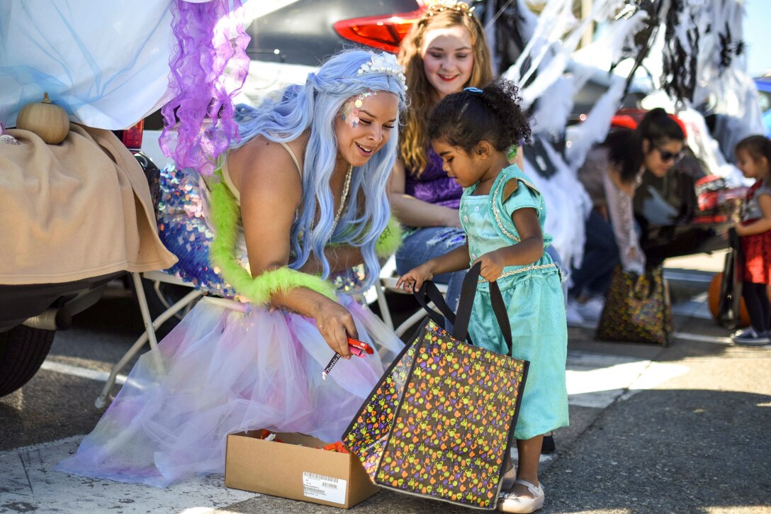 A woman dressed up like a princess gives candy to a little girl with a bag.