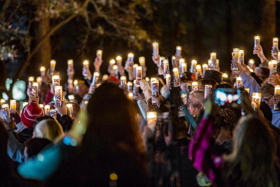Several dozen people raise candles in a dark night.