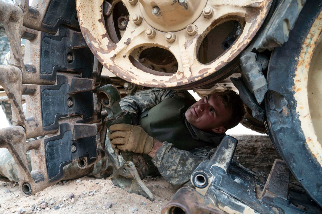 A soldier performs maintenance under a vehicle.