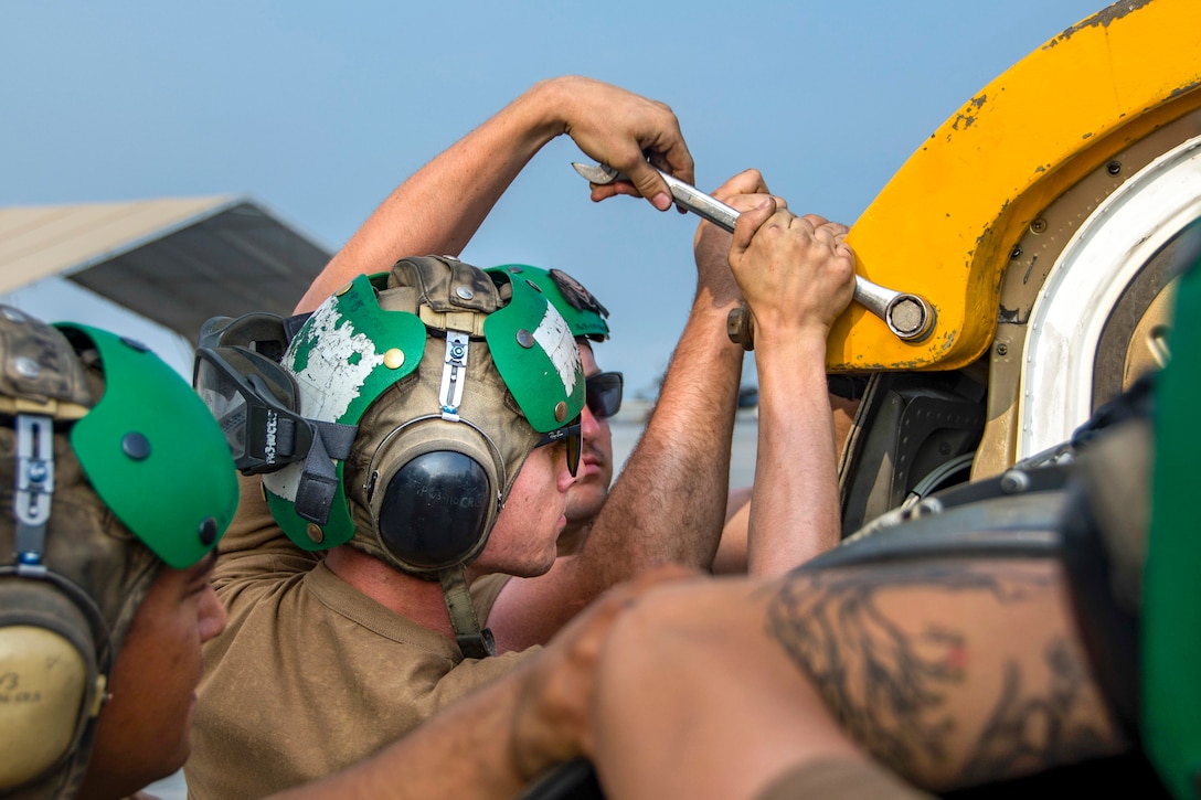 Sailors use a tool to remove a bolt from an aircraft part.