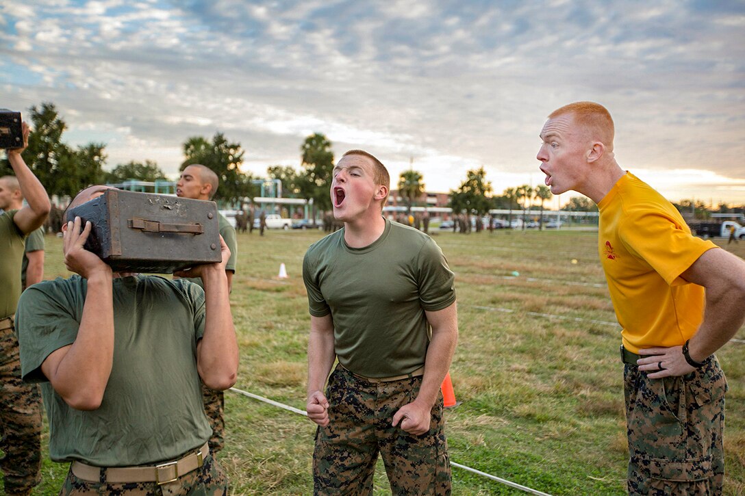 A drill instructor yells at a recruit carrying a box of ammunition outside.