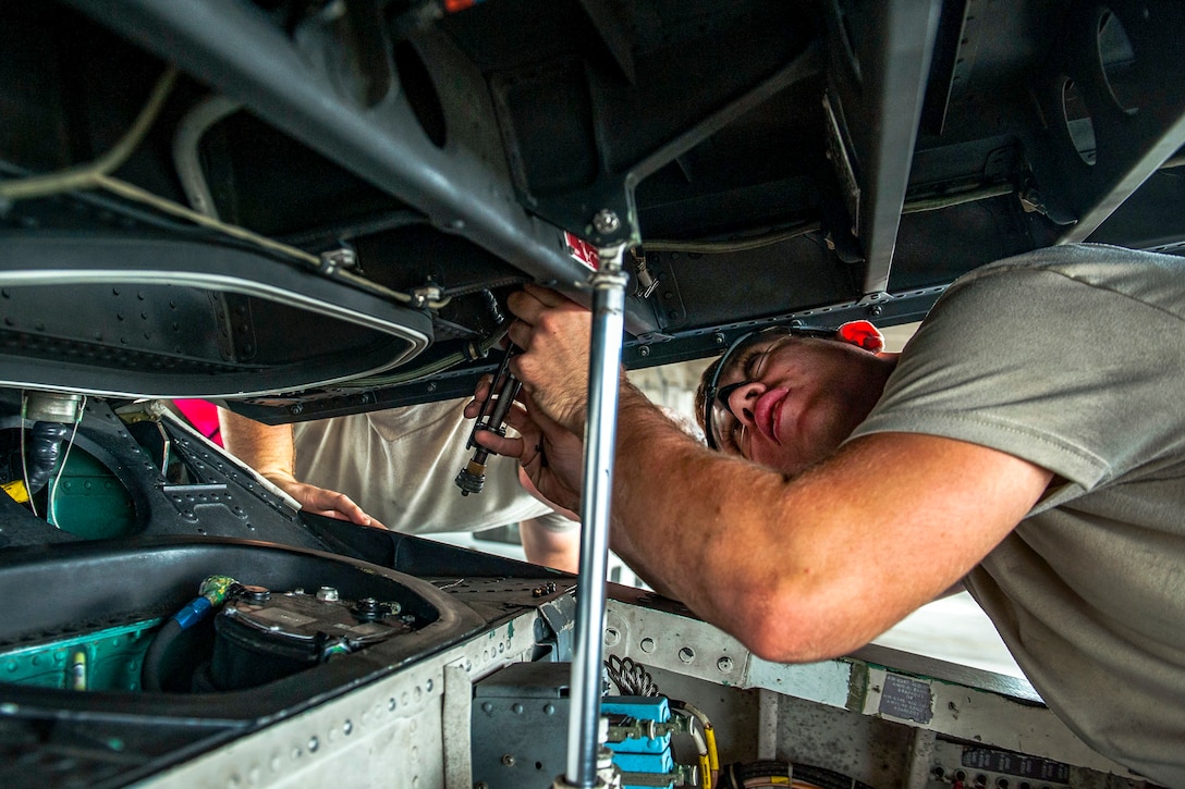 An airman works under the hood of an aircraft.