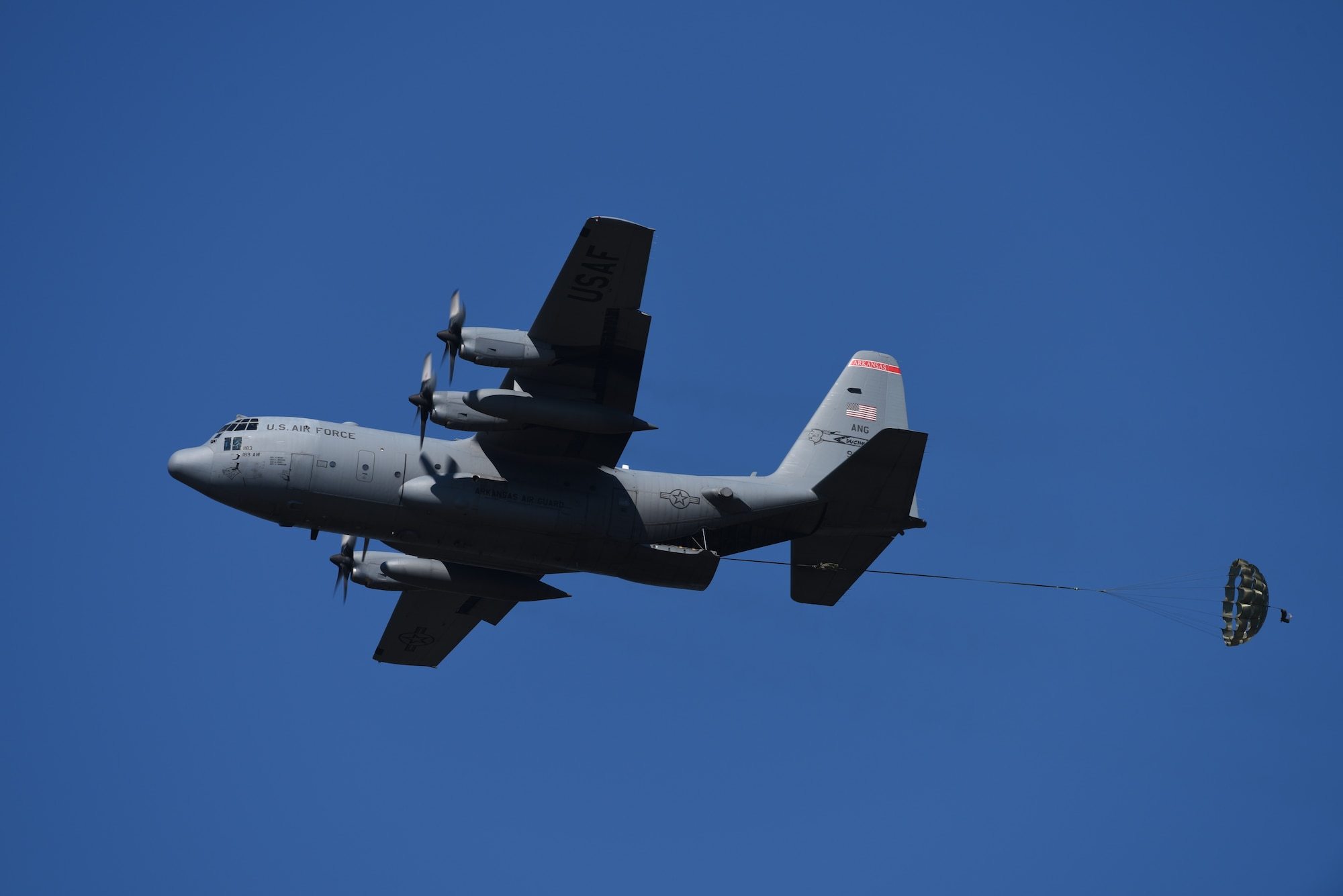 A gray C-130 releases cargo attached to a parachute