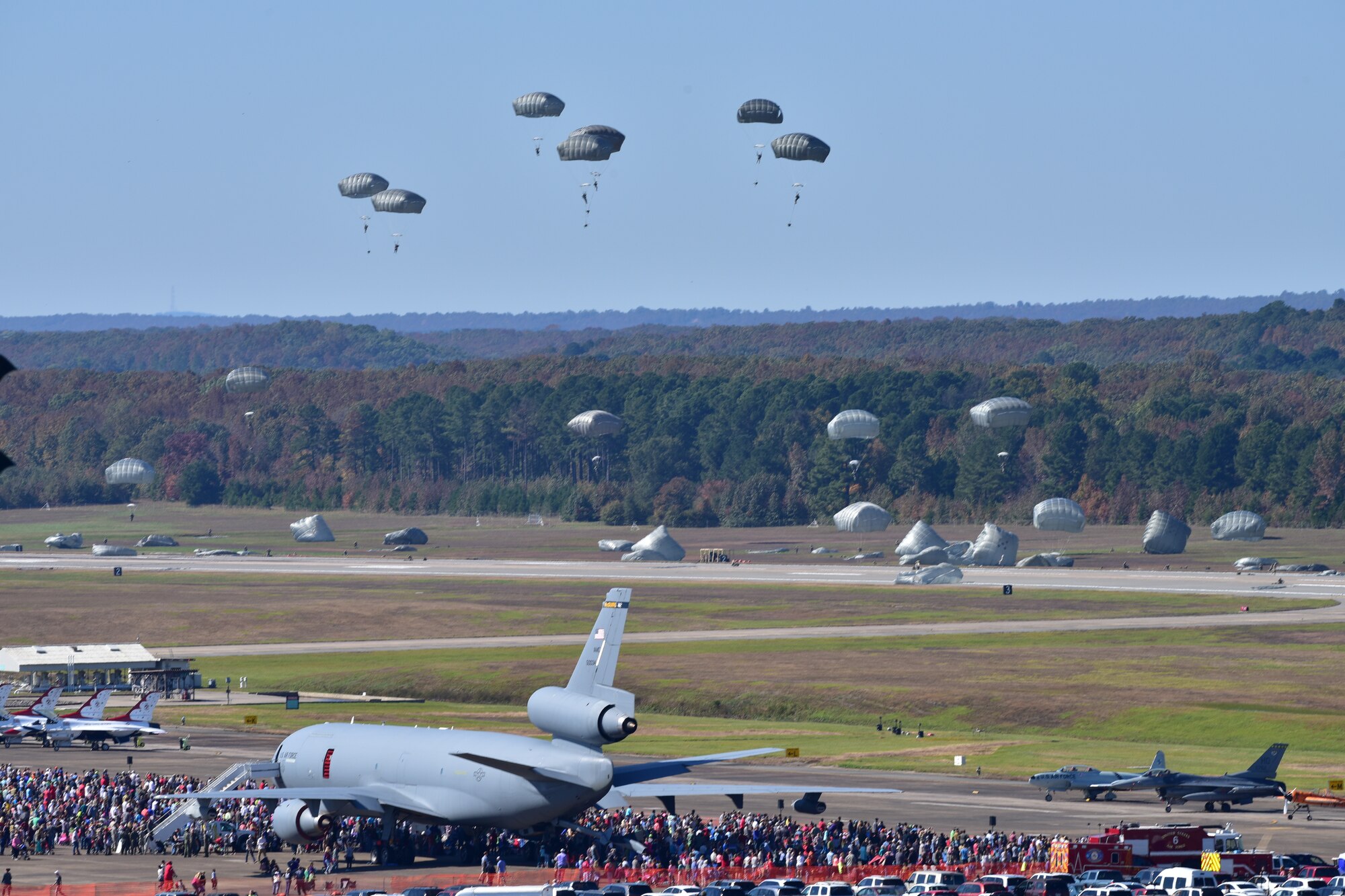 Parachutists glide from the sky onto a flightline during an airshow