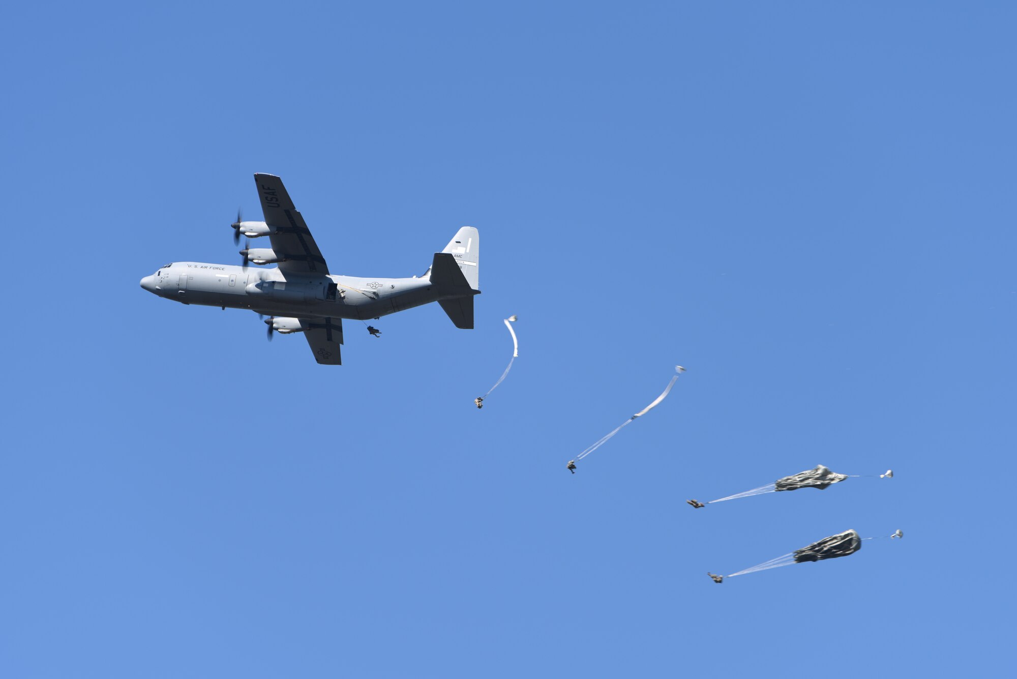 A gray C-130 drops parachutists mid air