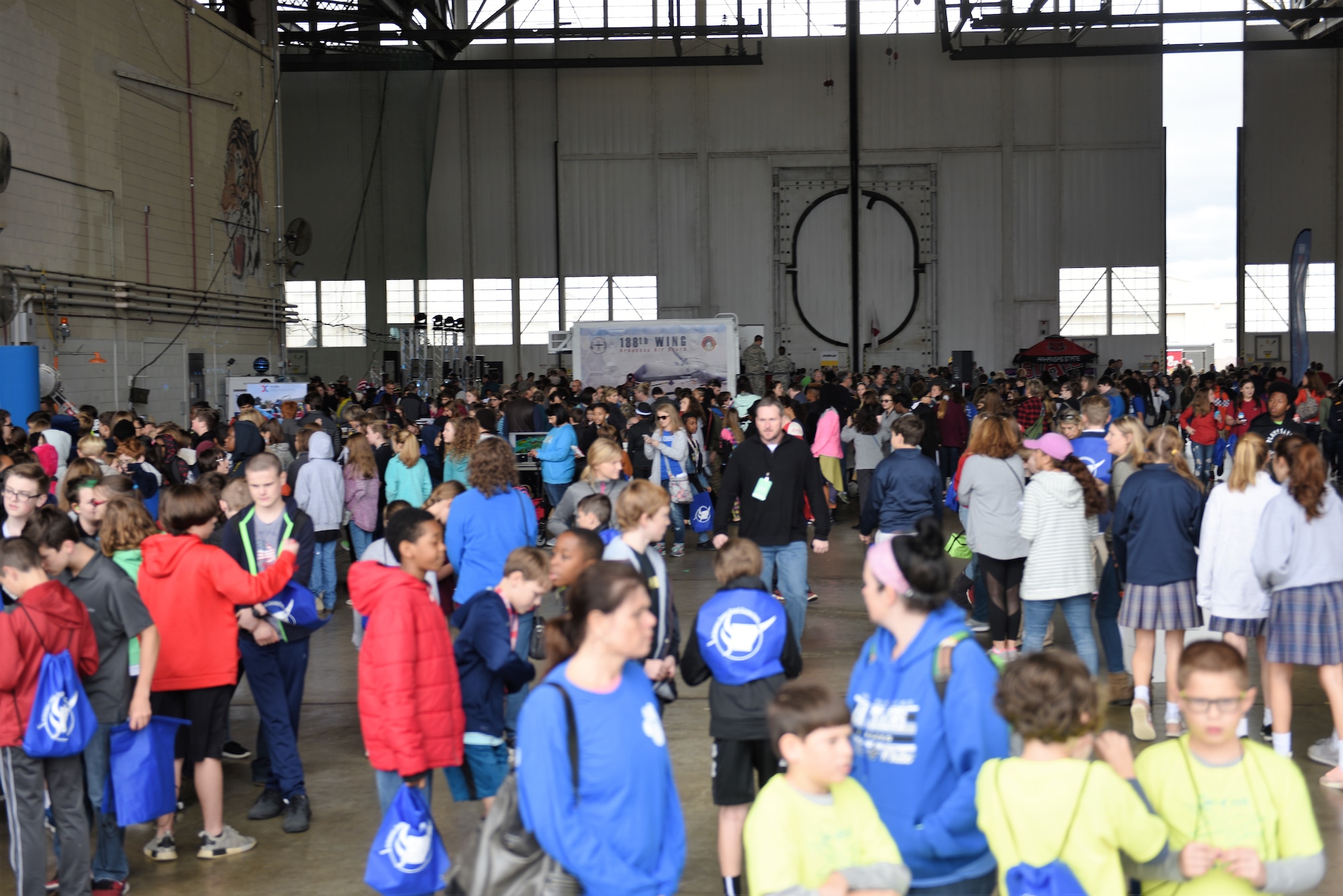 A crowd of school age children gather in an aircraft hangar